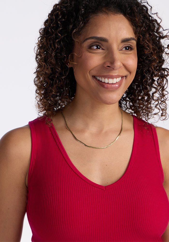 Curly-haired woman smiles in Woolx Vivi Ribbed Tank in Poppy Spark, with a gold necklace, on white background.