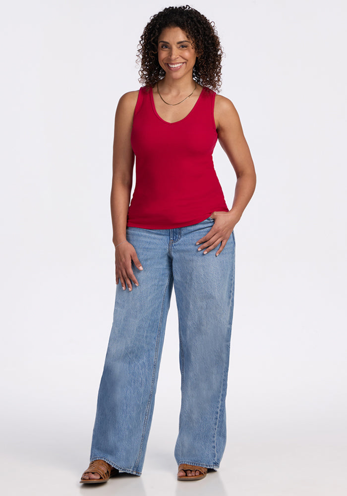 Smiling woman with curly hair wears Woolx Vivi Ribbed Tank in Poppy Spark, blue wide-leg jeans, and sandals.